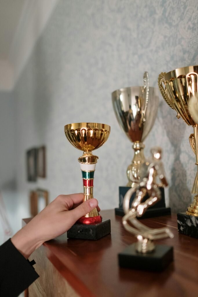 Close-up of various trophies on a shelf, with a hand holding one cup.