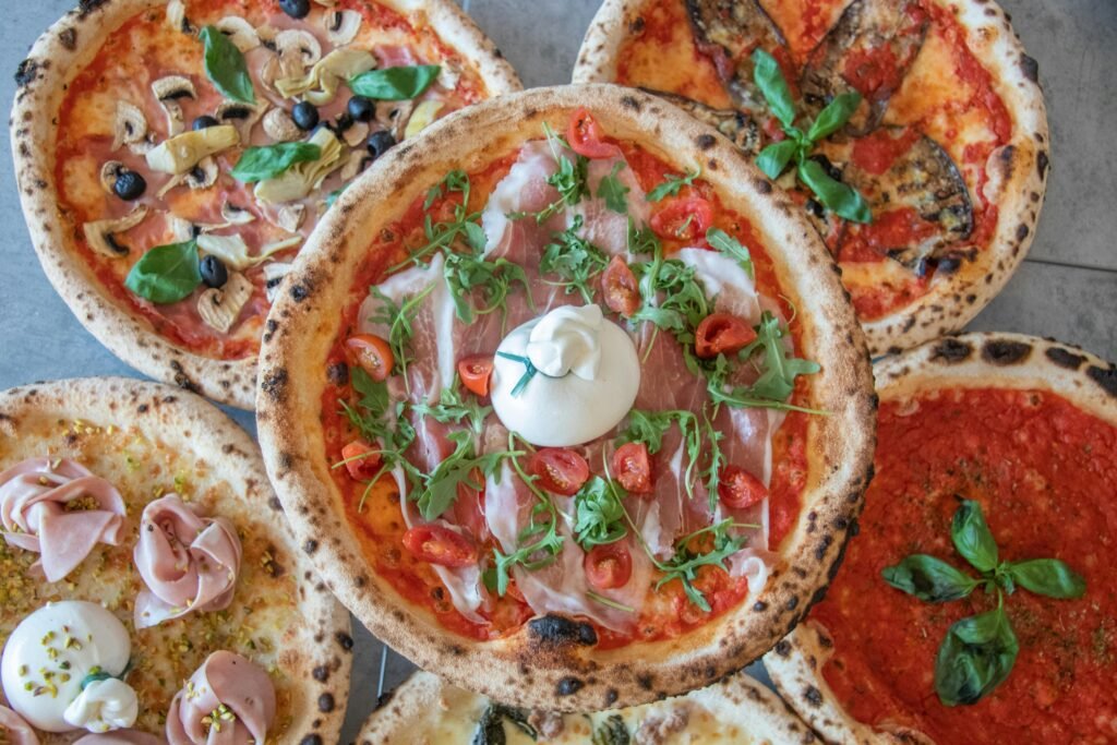 Top view of assorted gourmet pizzas with fresh toppings such as ham, cheese, and vegetables, perfect for food photography.