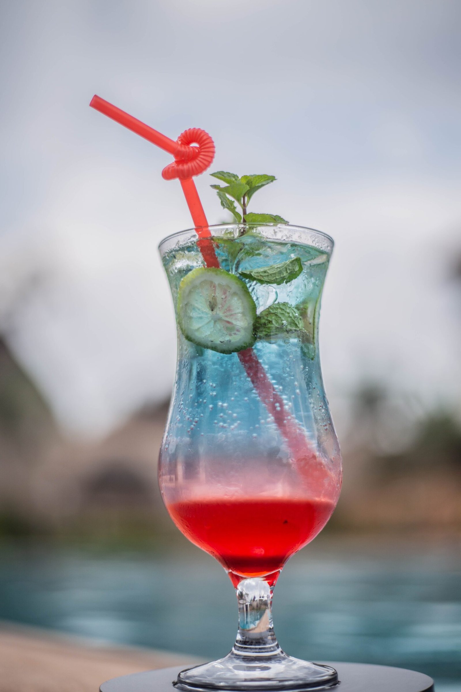 Vibrant tropical cocktail with mint, cucumber, and red straw by the poolside.