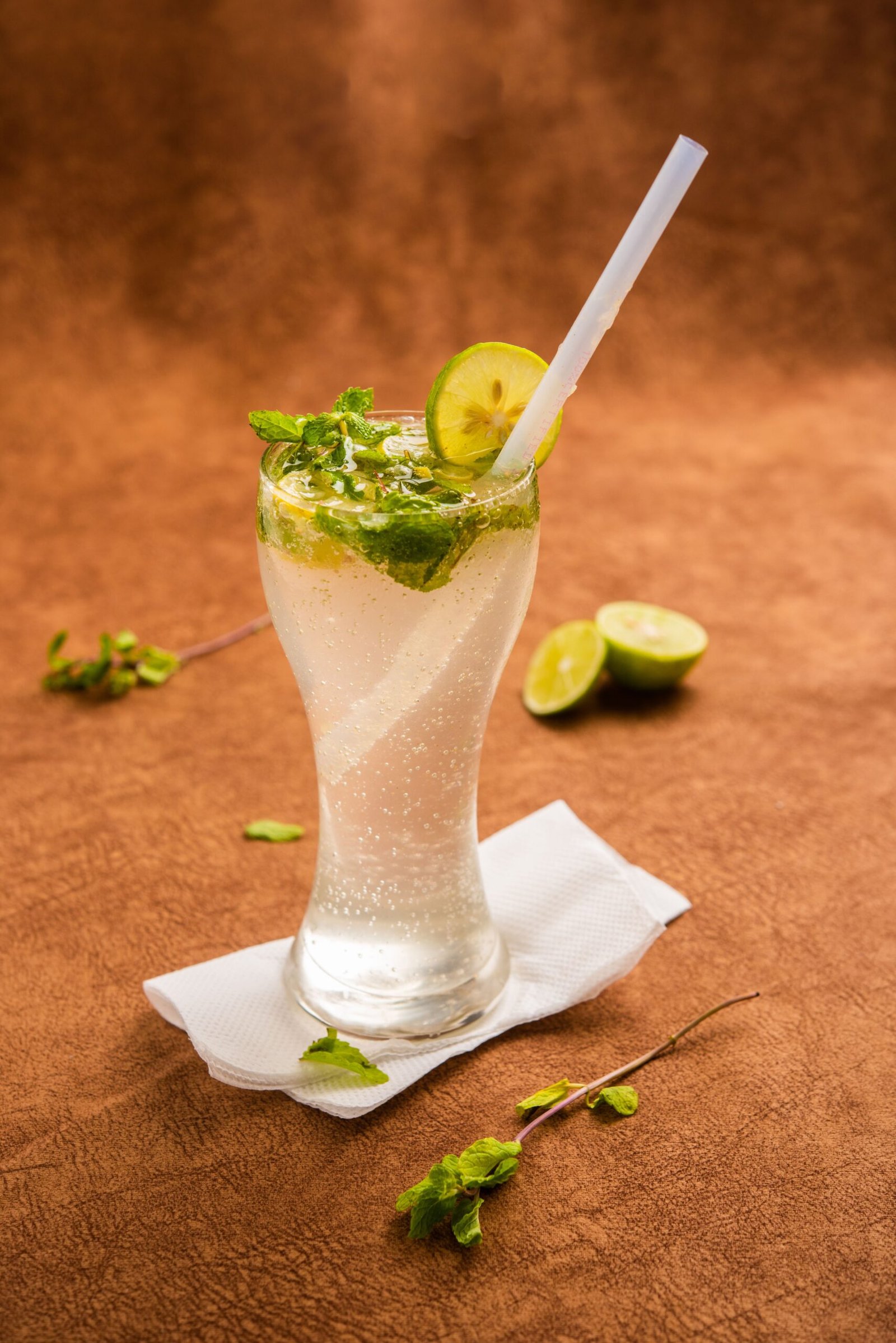 Tall glass of sparkling mojito garnished with lime and mint on a textured background.