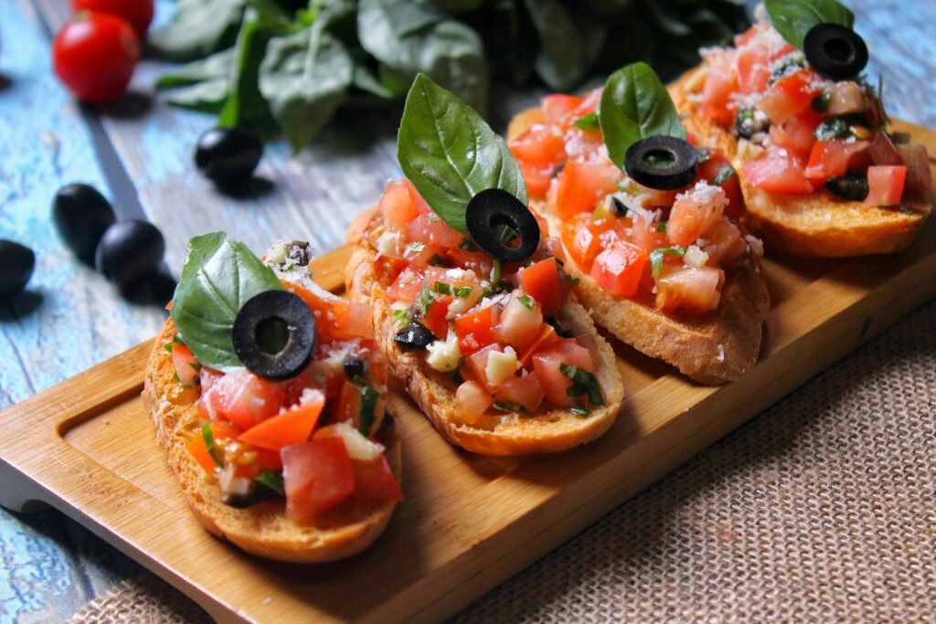 Freshly prepared Italian bruschetta with tomatoes, black olives, and basil on a cutting board.